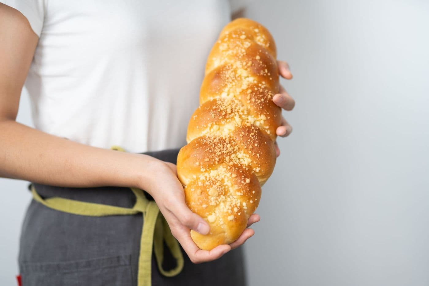 Close-up of a person holding a freshly baked braided challah bread indoors.